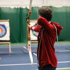 A man aiming a recurve bow at a target in Coombe Dingle. Links to Archery club page on Bristol SU Website